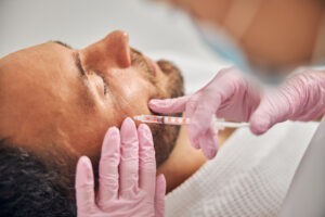 Close up of female cosmetologist in pink sterile gloves making injection in male forehead